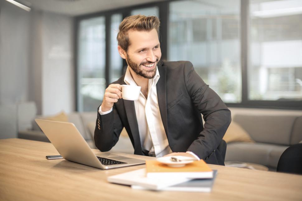 Free Image of Young Adult Man Holding White Teacup in Front of Gray Laptop 