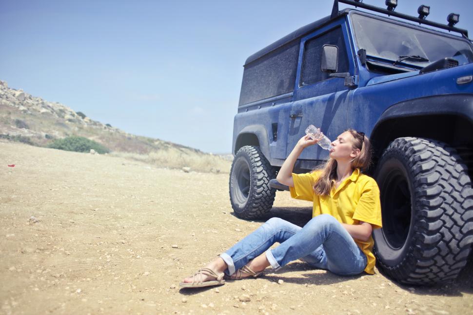 Free Image of Young Woman Drinking Water From Bottle While Sitting Besides SUV 