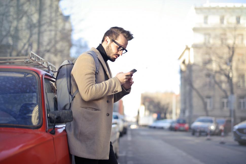 Free Image of Man in Beige Coat Holding Phone Leaning on Red Vehicle 