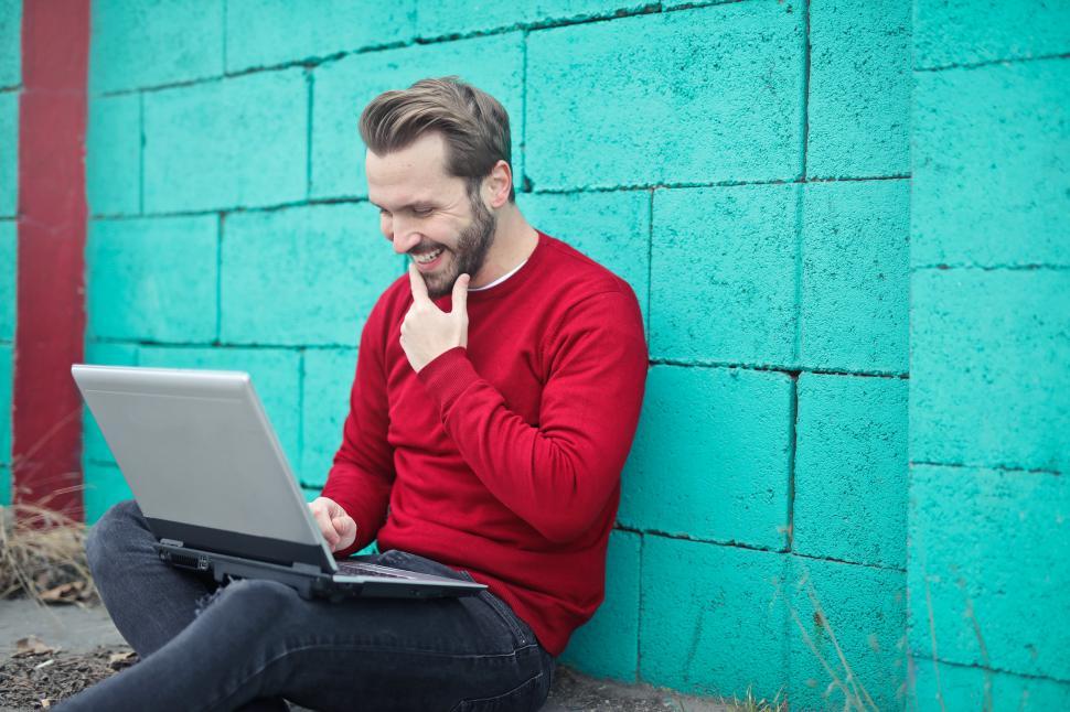 Free Image of Young Adult Man using a laptop against  turquoise brick wall 