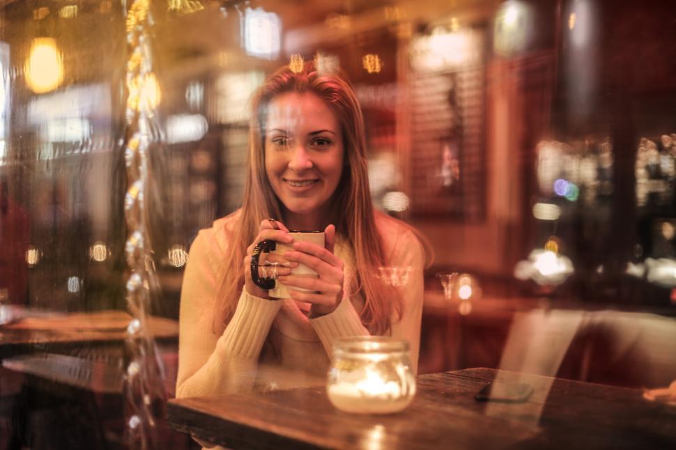 Free Image of Woman Smiling While Holding White Ceramic Cup Sitting Near Brown 