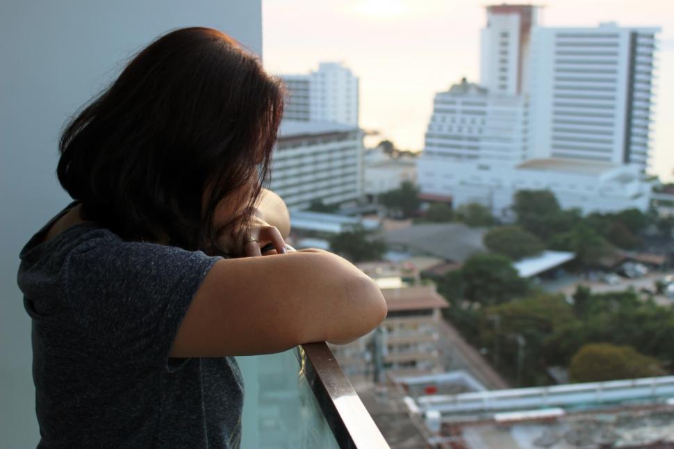 Free Image of A lady looks out at high-rise city buildings from a balcony  