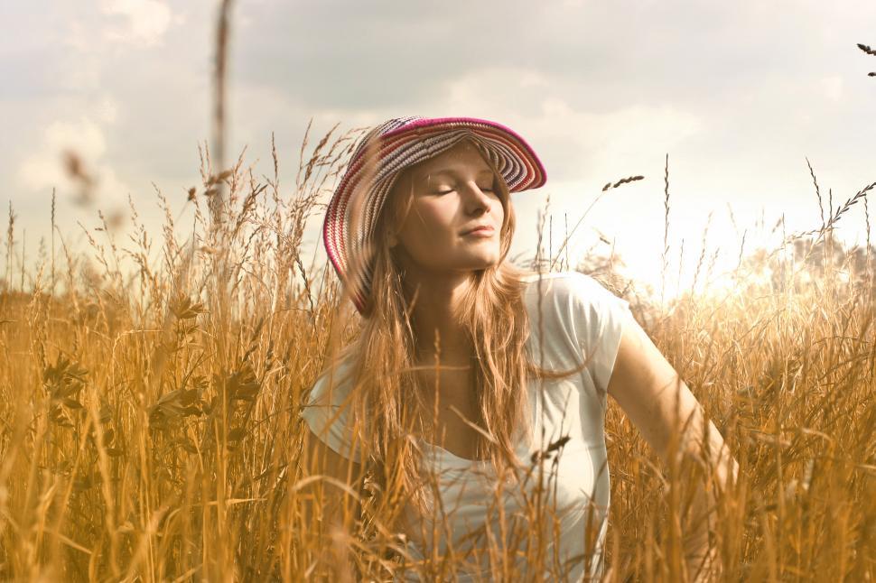 Free Image of Young woman in striped hat sitting with eyes closed in a wheat f 