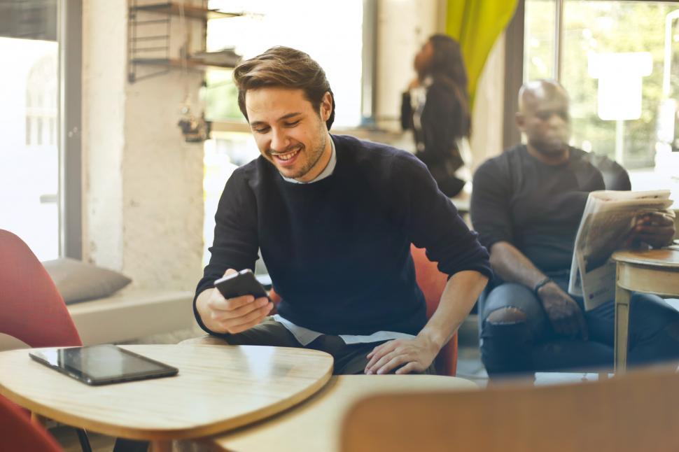 Free Image of Young Man Smiling While Using His Smartphone In Restaurant 