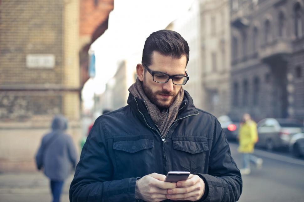 Free Image of Young Bearded Man Using His Smartphone To Text While Walking On 