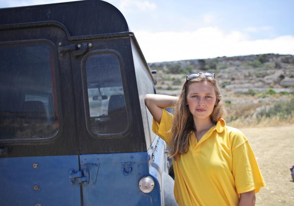 Free Image of Young Woman Posing Against Blue SUV 