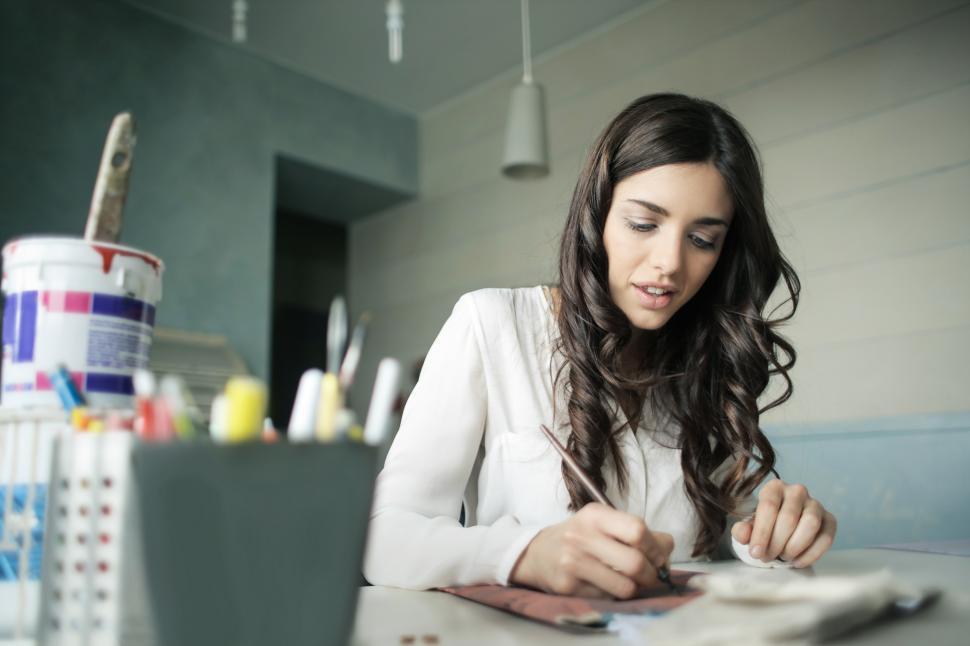 Free Image of A beautiful young woman writing on the papers at her desk 
