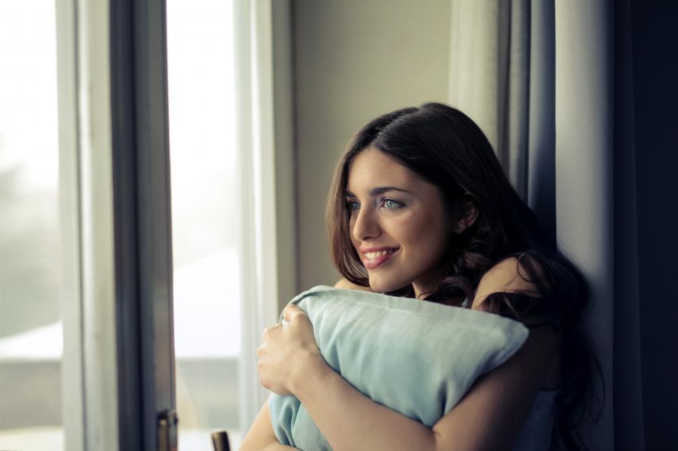 Free Image of A young brunette woman looks outside the window 