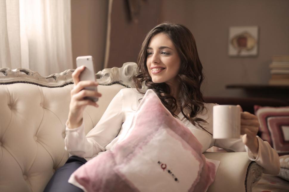 Free Image of A young woman looking at her mobile phone while holding a coffee 