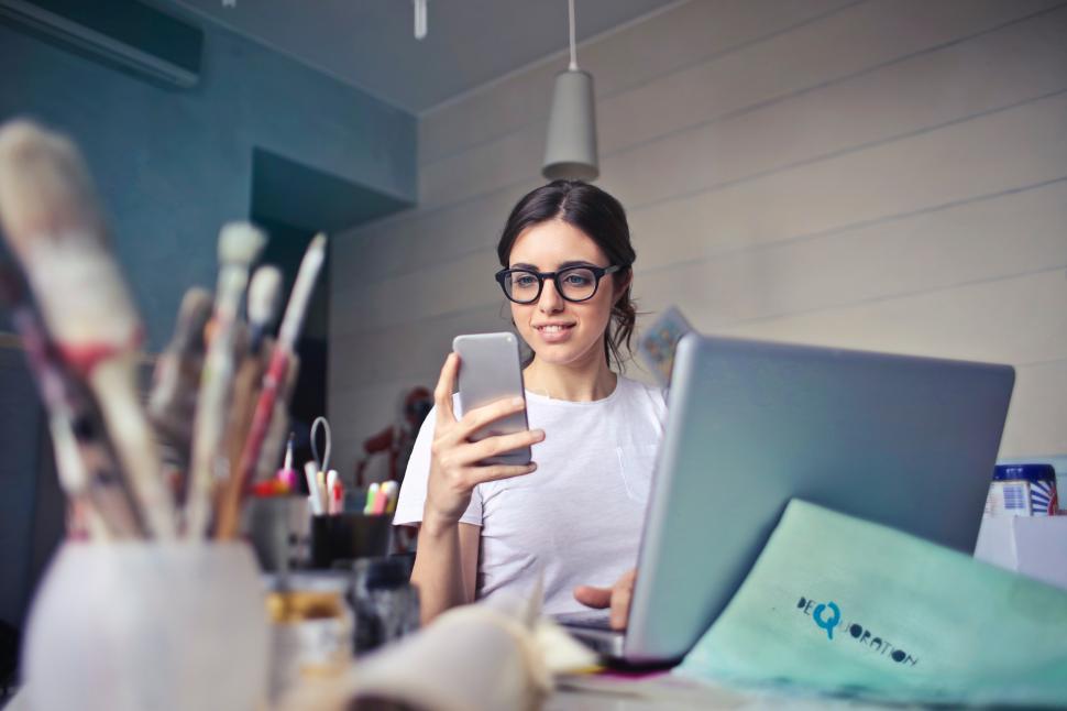 Free Image of A young woman working on her laptop looks at her mobile phone 