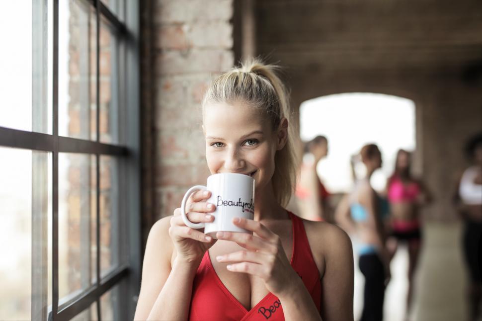 Free Image of A young blonde woman wearing red sports bra holding coffee mug i 