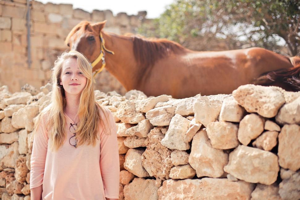 Free Image of A teenage blonde girl standing outside a horse ranch 
