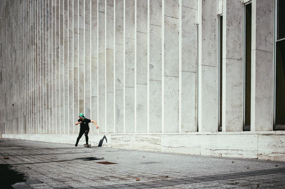Free Image of A young caucasian skateboarder rides past a city building 