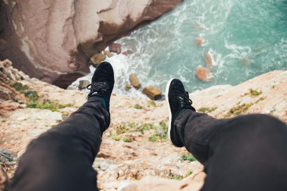 Free Image of Feet hanging over the edge of a layered rock 