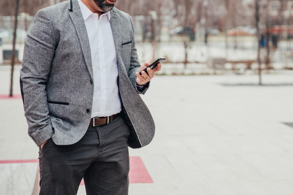 Free Image of A businessman looks at mobile phone outdoors 