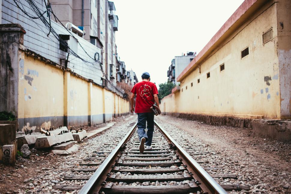 Free Image of A young skateboarder walking on train tracks 