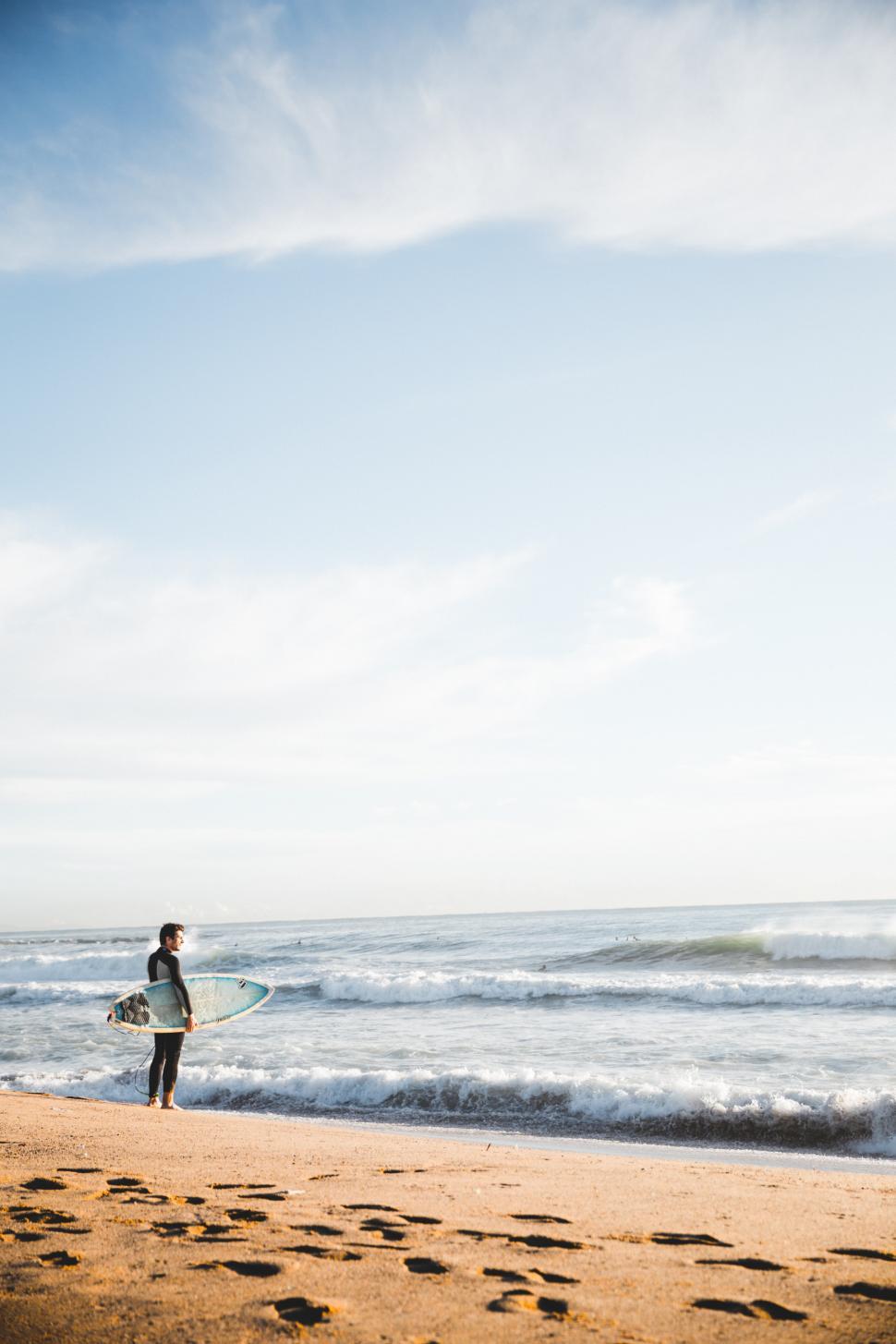 Free Image of A young Caucasian surfer carrying surfboard on the beach 