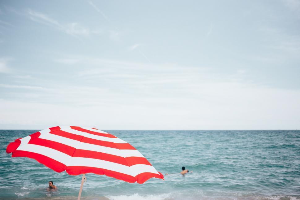 Free Image of A beach umbrella and people swimming 
