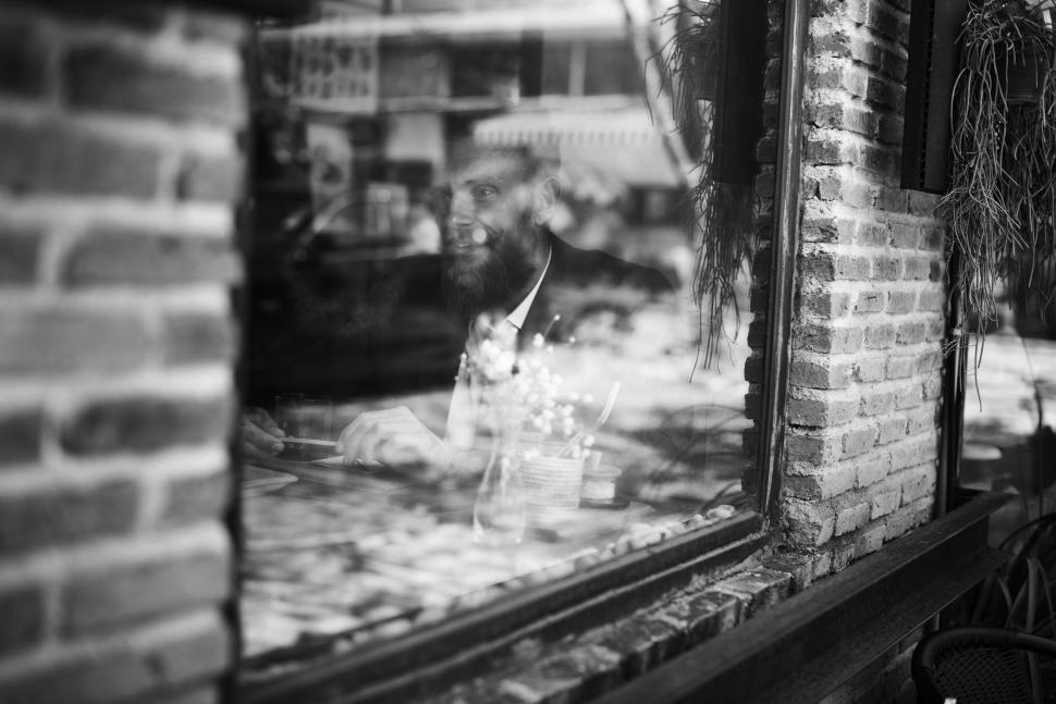 Free Image of Black and white photograph of a bearded man sitting at a restaur 