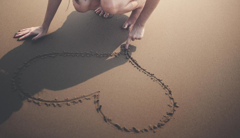 Free Image of A young woman s hand drawing a heart in the sand 