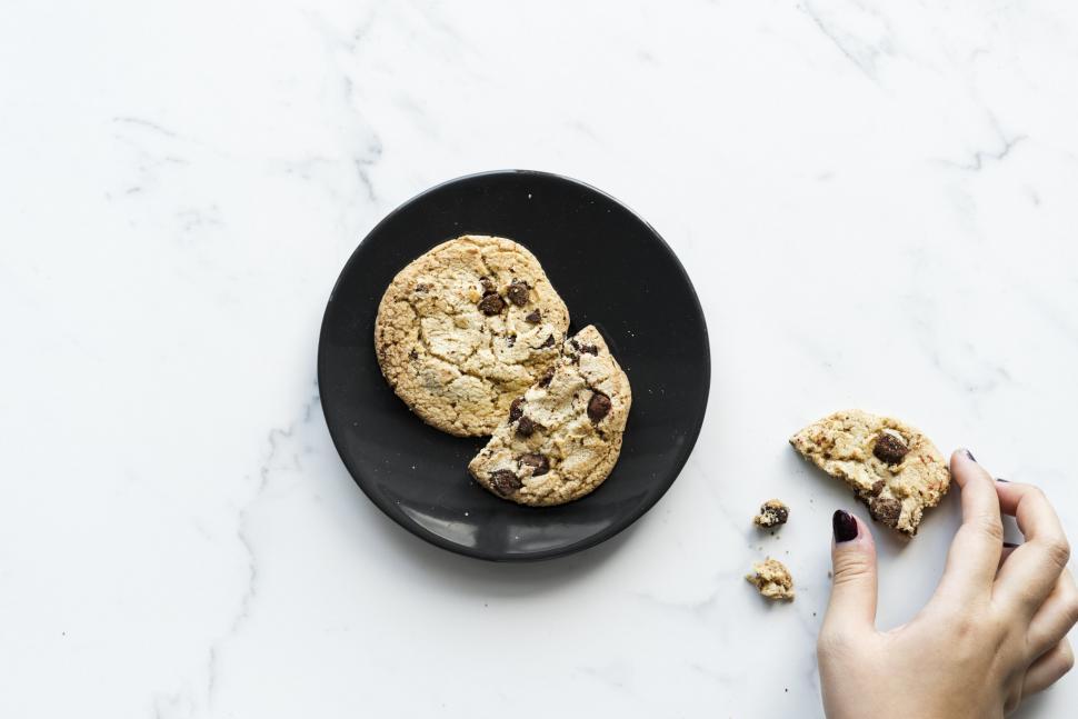Free Image of Womans hand picking up a piece of chocolate chip cookie 
