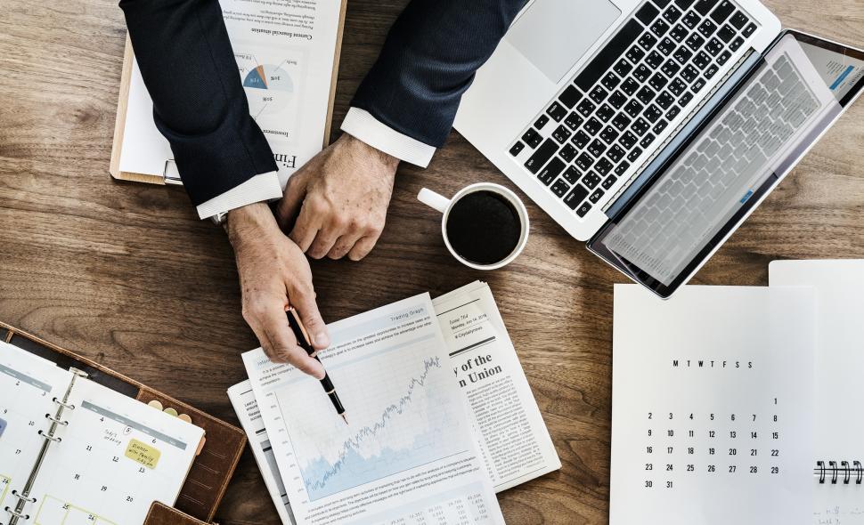 Free Image of Flat lay of a hands pointing at trending graph with a pen on the paper 