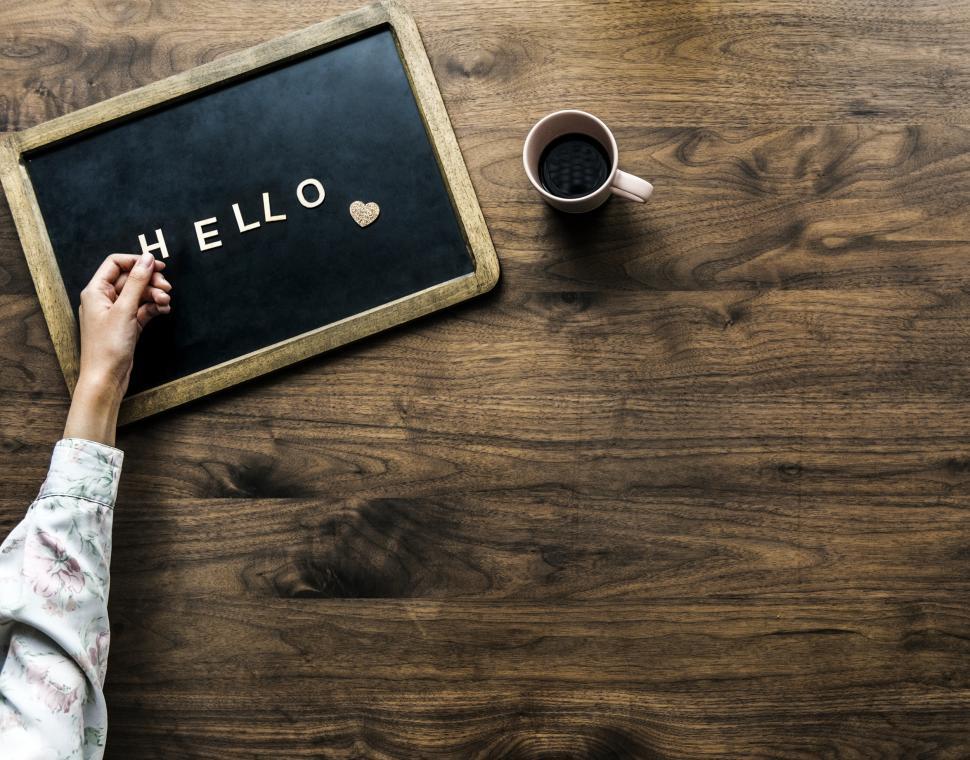 Free Image of Flat lay of a hand arranging the text HELLO on a slate blackboard 