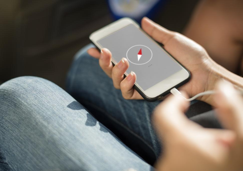 Free Image of Close up a mobile phone in a hand being charged and a compass symbol on its screen 