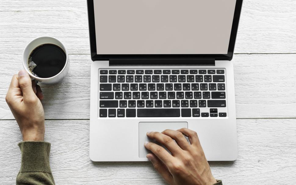 Free Image of Close up of a hand holding coffee working at computer workspace 