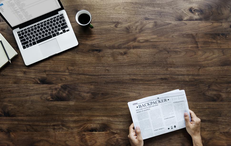 Free Image of Overhead view of hands reading a newspaper at the table with computer 