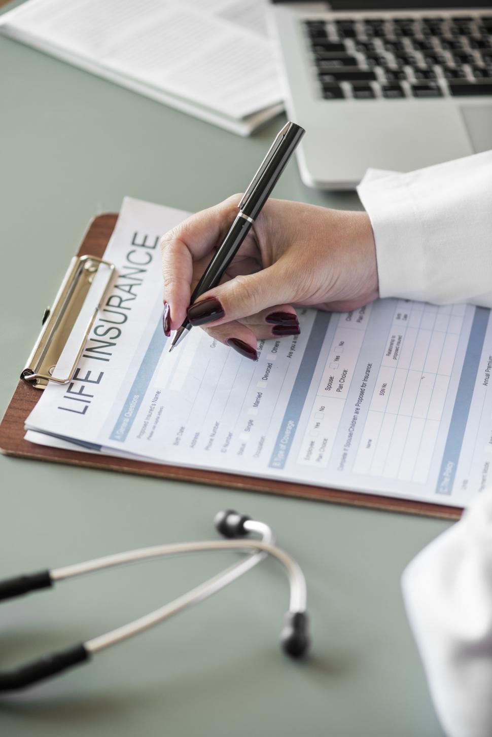 Free Image of Close up of a doctor s hand writing on the insurance questionnaire 
