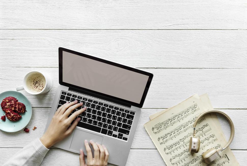 Free Image of Close up of a person s hands typing on laptop alongside music notes and a headphone 