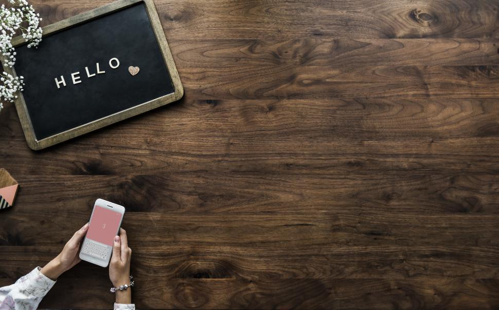 Free Image of Overhead view of the word HELLO on a slate board and hands holding mobile phone 