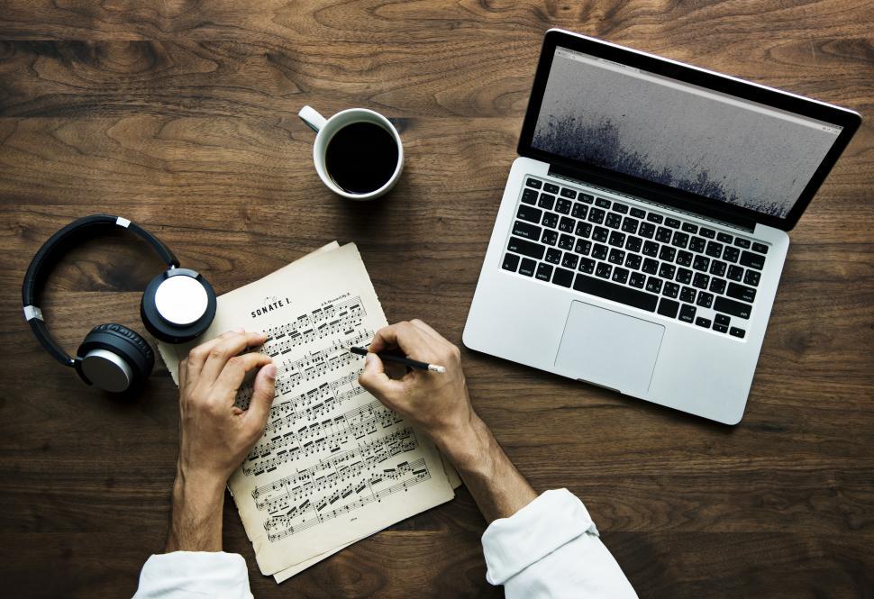 Free Image of Overhead view of a person s hand writing musical notes on a sheet of paper 