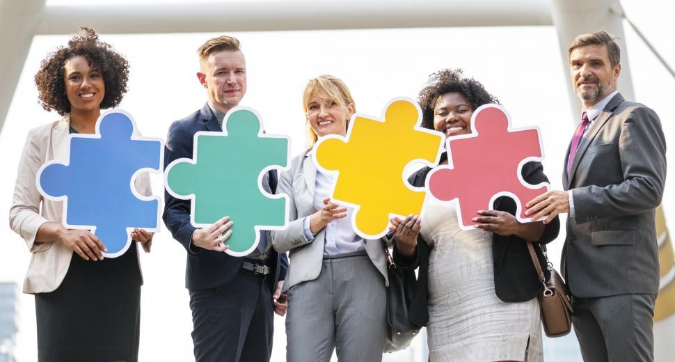 Free Image of A group of colleagues holding cardboard jigsaw puzzle cutouts 