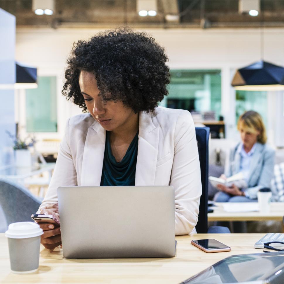 Free Image of A young woman looking at her mobile phone at her office 