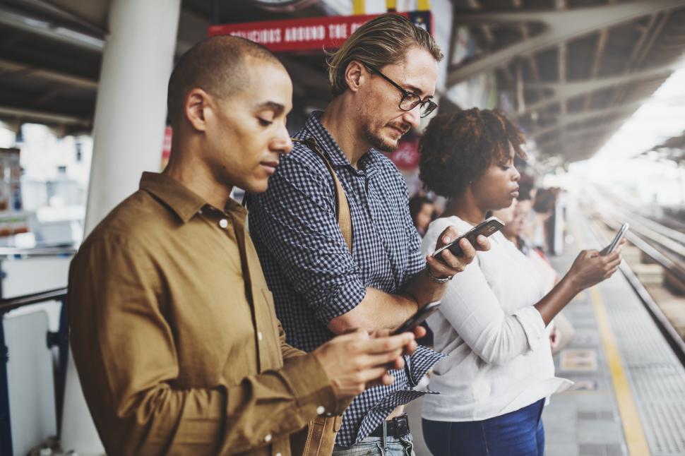 Free Image of Commuters looking at their mobile phones on a train platform 