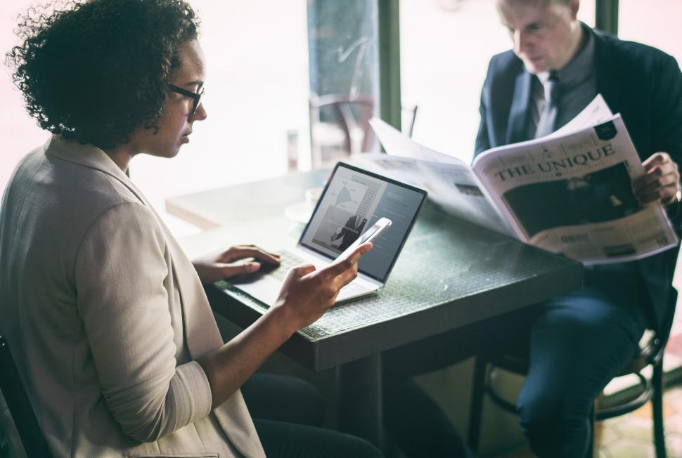 Free Image of Two businesspeople at a cafe on phone and reading paper 