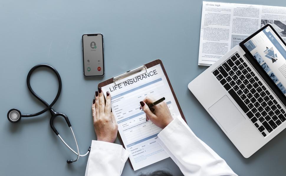 Free Image of Overhead view of a doctor s hand writing on life insurance questionnaire 