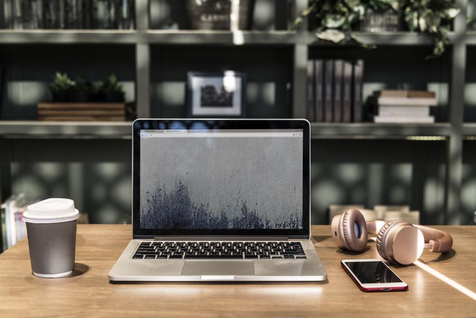Free Image of A laptop surrounded with a disposable coffee mug and a smart phone 