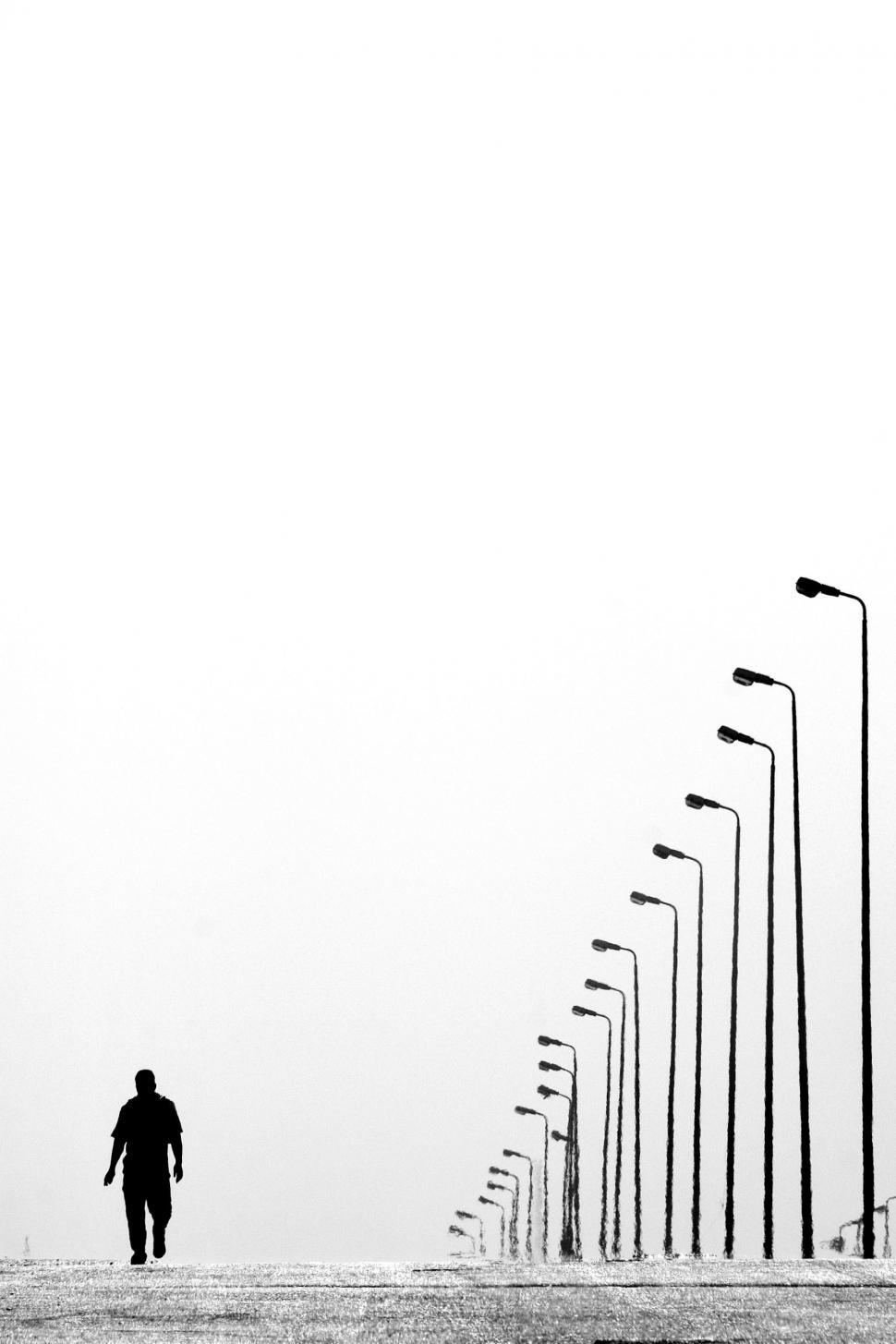 Free Image of Silhouette of walking man besides row of lamp posts  