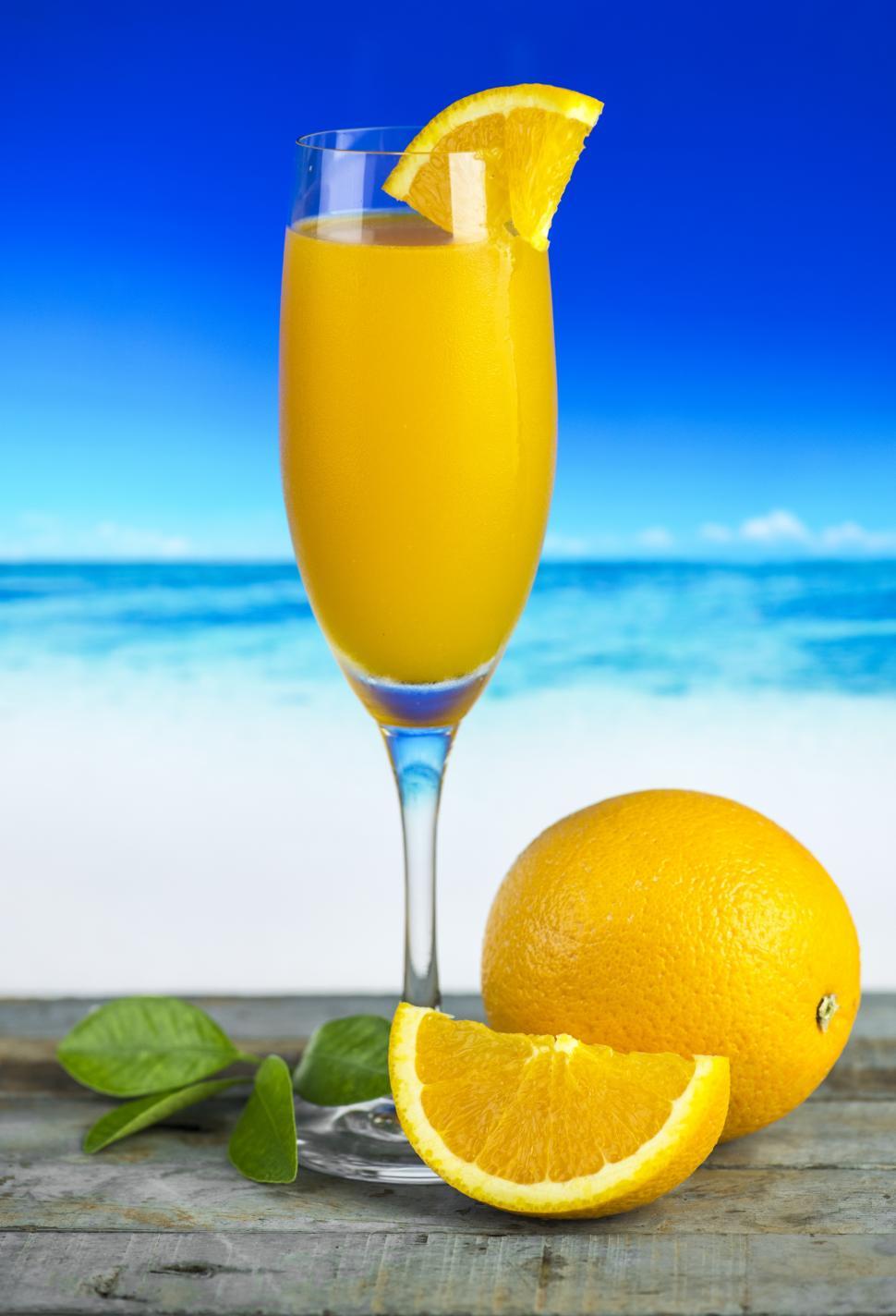 Free Image of Close up of orange juice in a glass, beach scene 