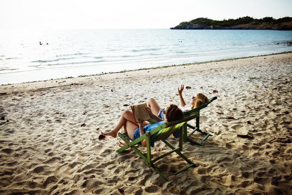 Free Image of A young woman reading book with a friend on the beach 