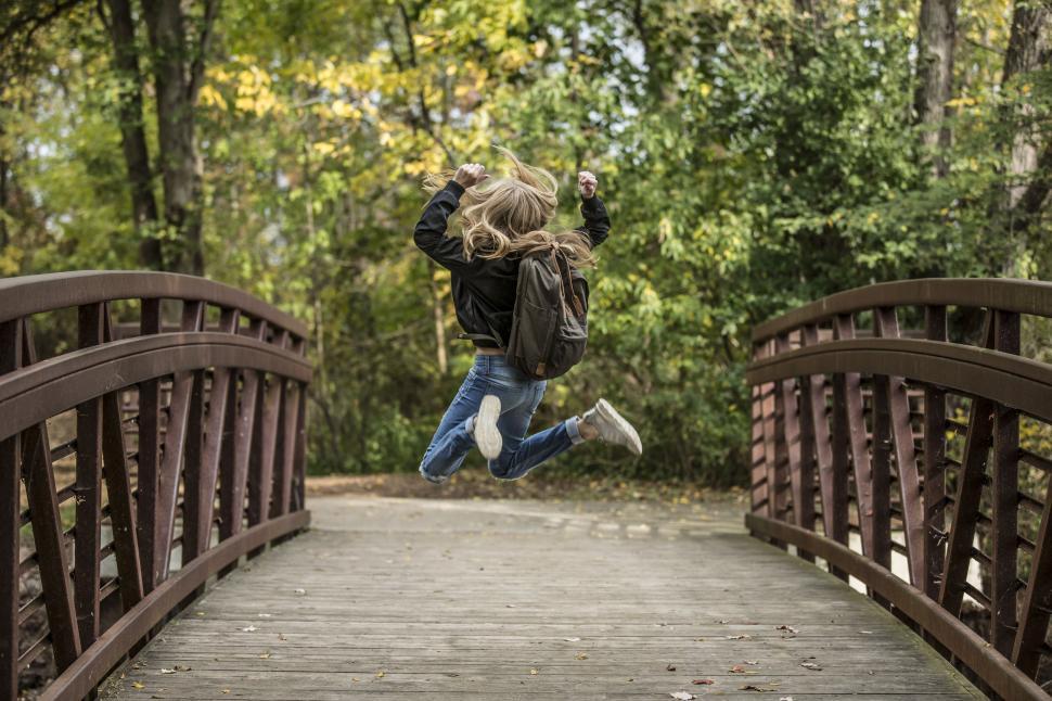 Free Image of Blonde Girl Jumping on Pedestrian Bridge 