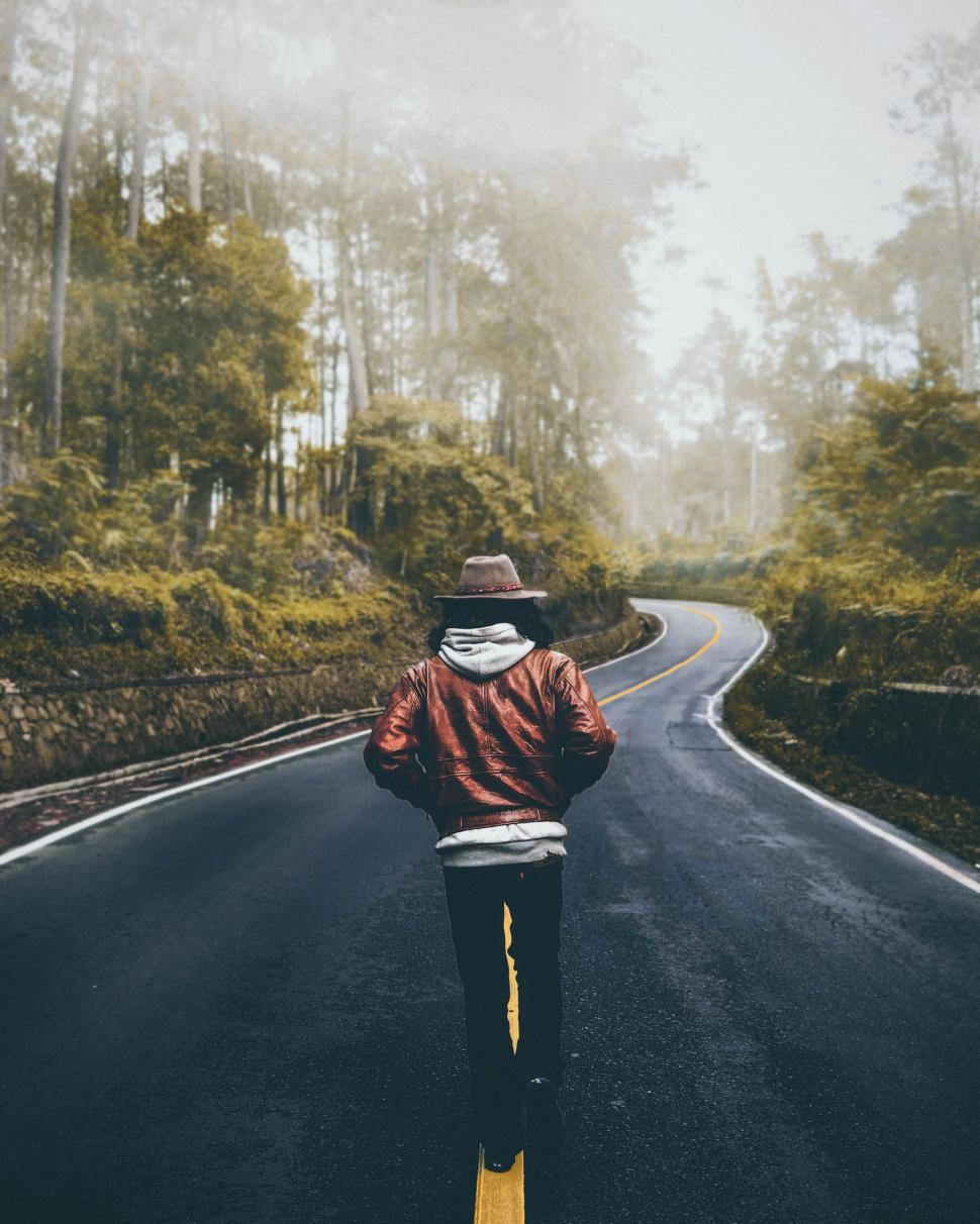 Free Image of Back View of Man in hat on road with trees and fog  