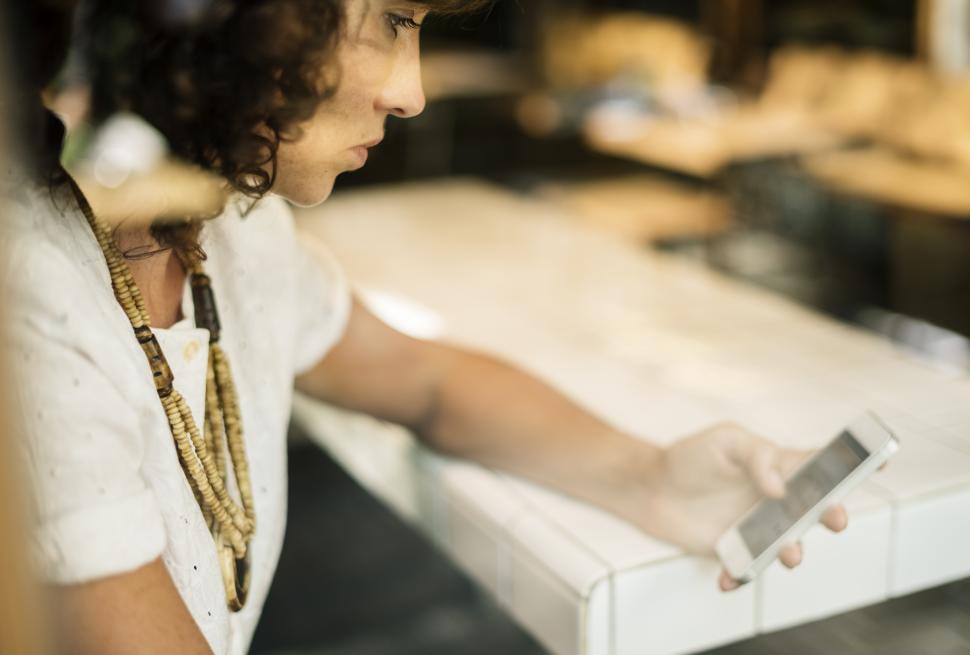 Free Image of A young woman looking at her mobile phone, alone at a table 