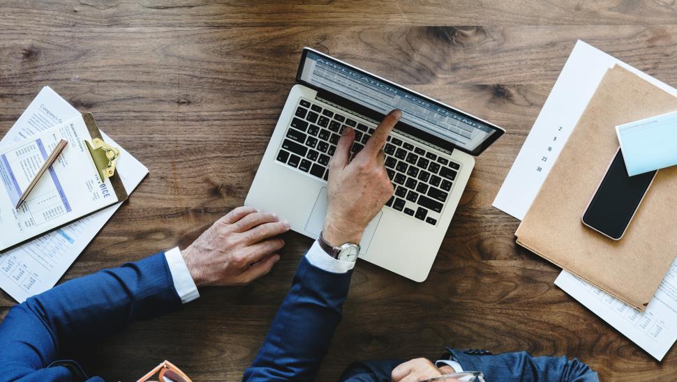 Free Image of Overhead view of two people looking at a laptop screen, pointing 
