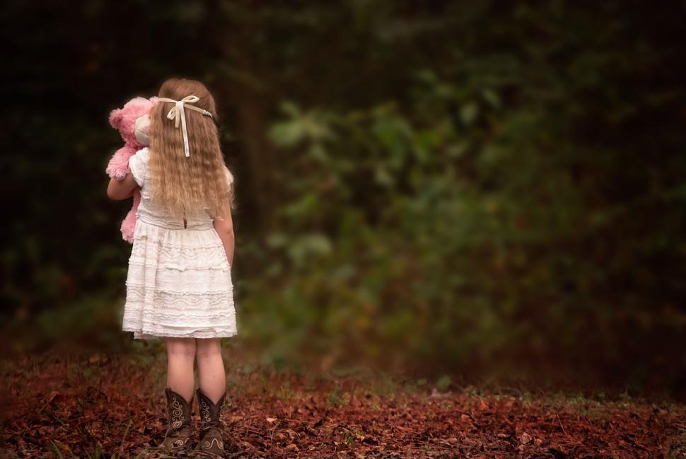 Free Image of Little Girl in White Dress Standing With Teddy Bear 