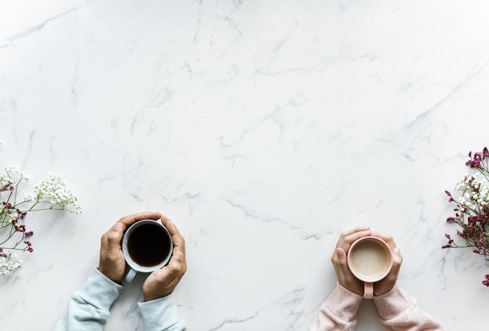 Free Image of Overhead view of two sets of hands holding coffee mugs in their palms 