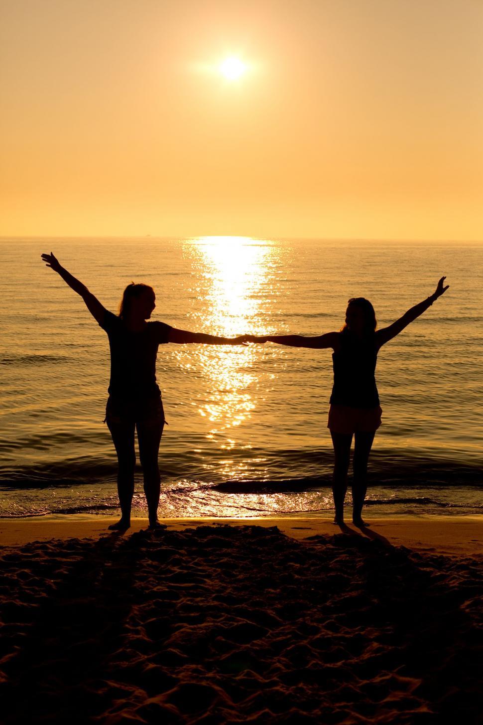 Free Image of Two girls dancing with ocean and sunset in the background  